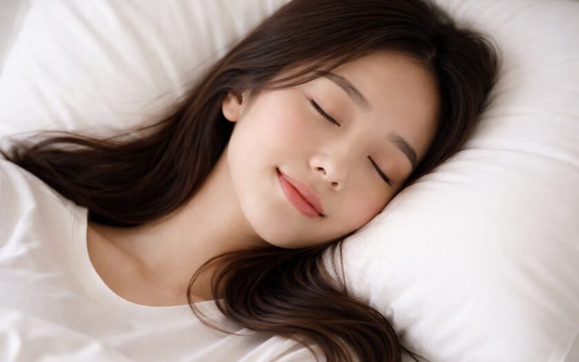 ผู้หญิงเอเชียนอนหลับบนหมอนสีขาวอย่างสบาย เห็นเฉพาะช่วงบน แสงนุ่มเป็นธรรมชาติ